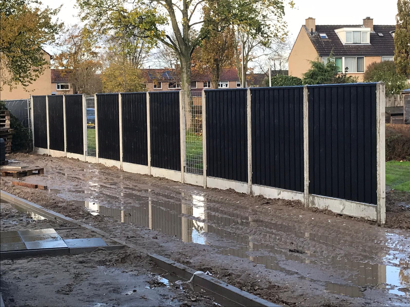 Zwarte houten schutting met betonnen palen langs nieuwe straat